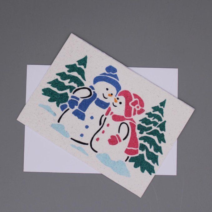 Carte de Noël montrant deux bonshommes de neige en sable, entourés de sapins.