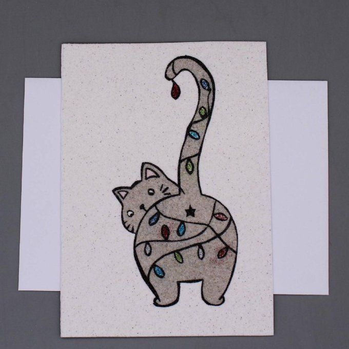 Carte de Noël en sable représentant un chat gris entouré de guirlandes lumineuses.