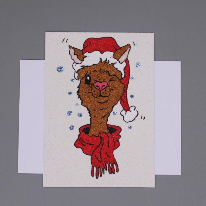 Carte de Noël représentant un lama souriant avec bonnet et écharpe, réalisée en sable.
