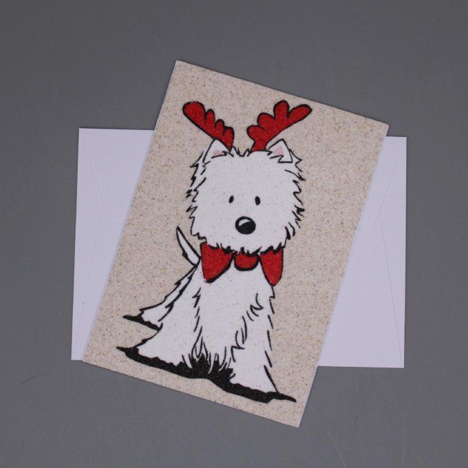 Carte de Noël en sable représentant un chien blanc avec des bois de renne et un nœud papillon rouge.