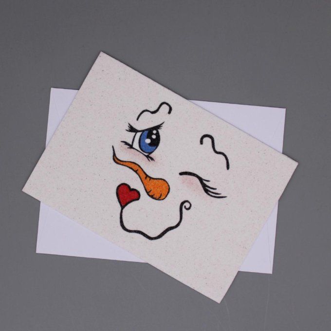 Carte de vœux en sable représentant le visage d’un bonhomme de neige clin d’œil.