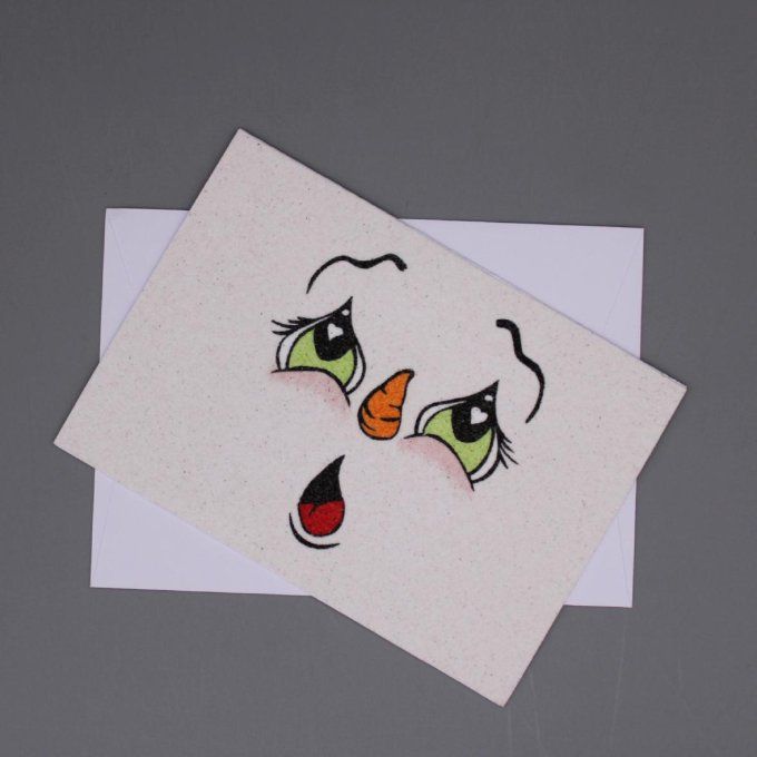 Carte de Noël en sable représentant un bonhomme de neige surpris, aux grands yeux verts.