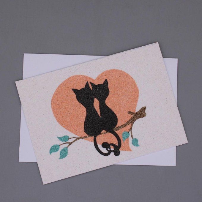 Carte de vœux en sable représentant deux chats noirs enlacés sur une branche, avec un grand cœur en