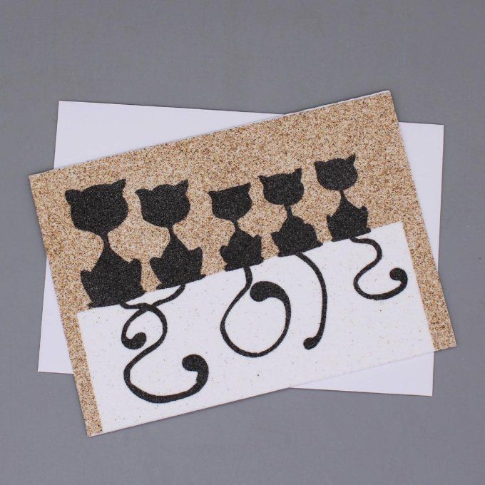 Carte de vœux en sable montrant cinq silhouettes de chats noirs alignés sur un mur.