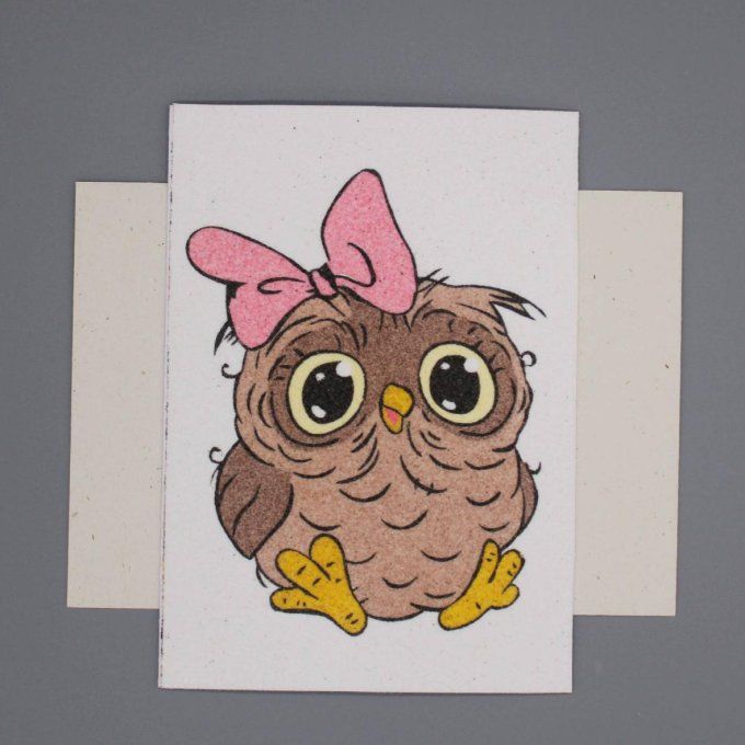 Carte de vœux en sable représentant une chouette brune avec un nœud rose sur la tête.