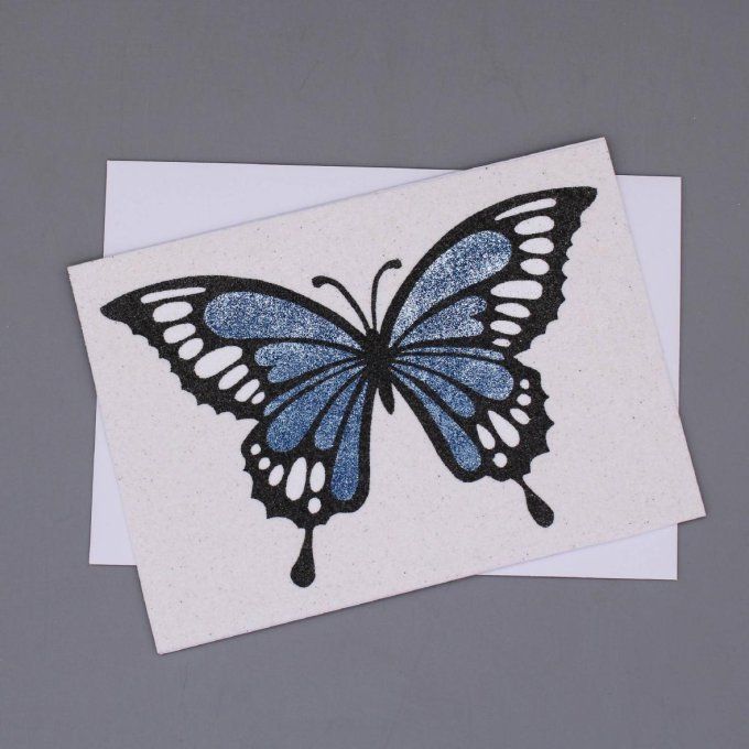 Carte de vœux en sable représentant un papillon noir aux ailes bleues scintillantes.