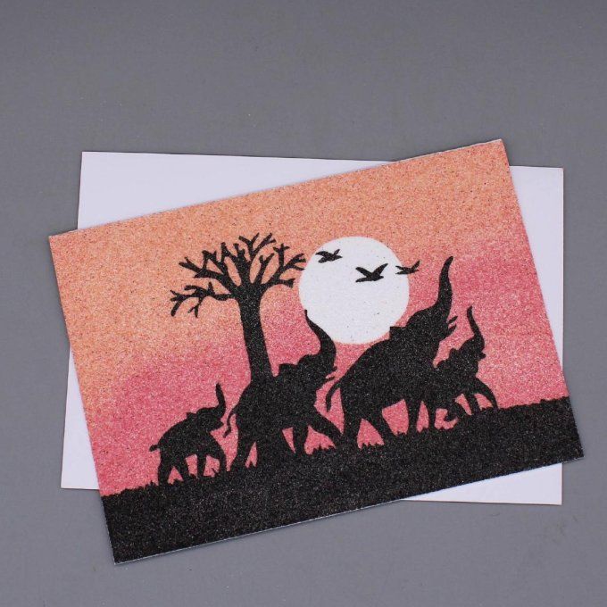 Carte de vœux en sable montrant des éléphants et un baobab devant un coucher de soleil rose et orang
