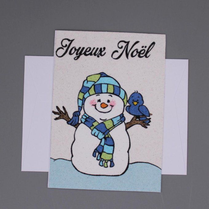 Carte de Noël en sable représentant un bonhomme de neige souriant avec un oiseau sur son bras et l’i