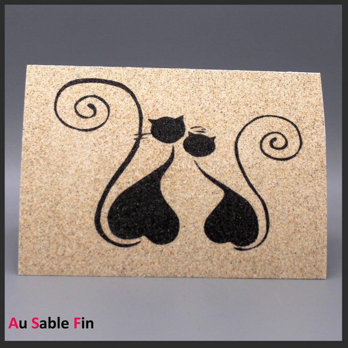 Carte en sable représentant deux chats noirs formant un cœur avec leurs silhouettes.