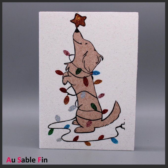 Carte de Noël en sable représentant un chien debout entouré de guirlandes lumineuses, tenant une éto