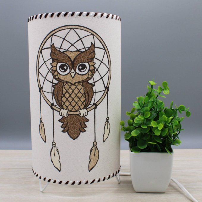 Lampe cylindrique en sable “Attrape-rêves hibou” dans un décor neutre