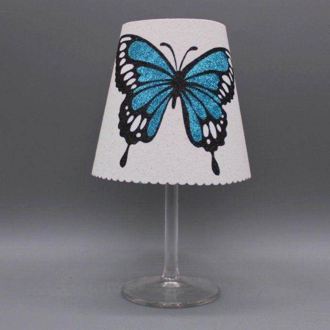 Photophore artisanal « Papillon ailes ouvertes » avec paillettes colorées turquoise sur fond blanc.
