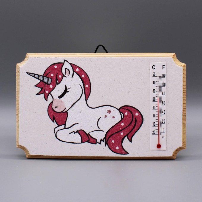 Thermomètre "Licorne" illustrant une licorne couchée avec paillettes sur fond de sable blanc.